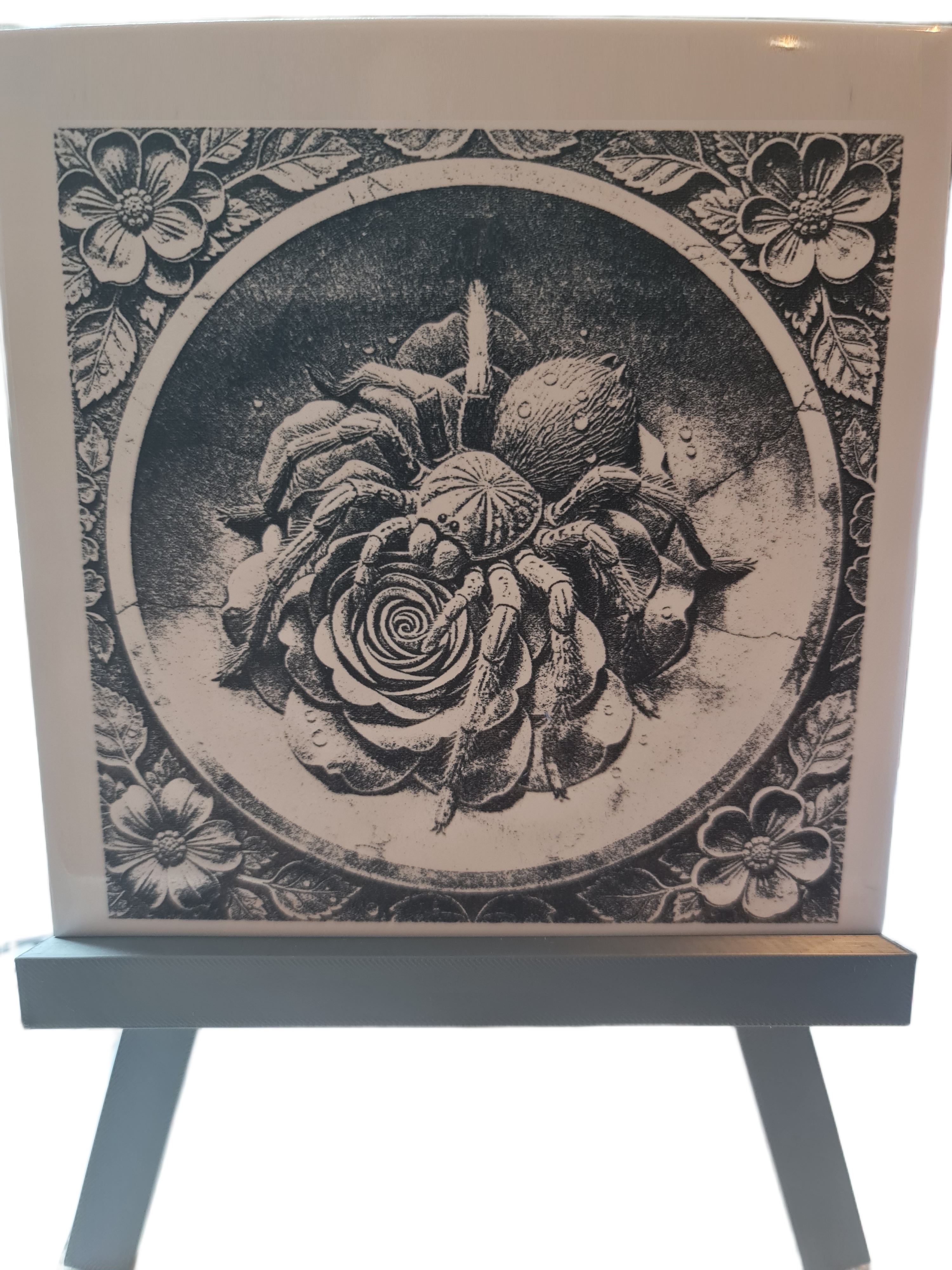 Intricate black and white drawing of a spider and rose in a floral circle, on display at Acier Manufacturing Limited.